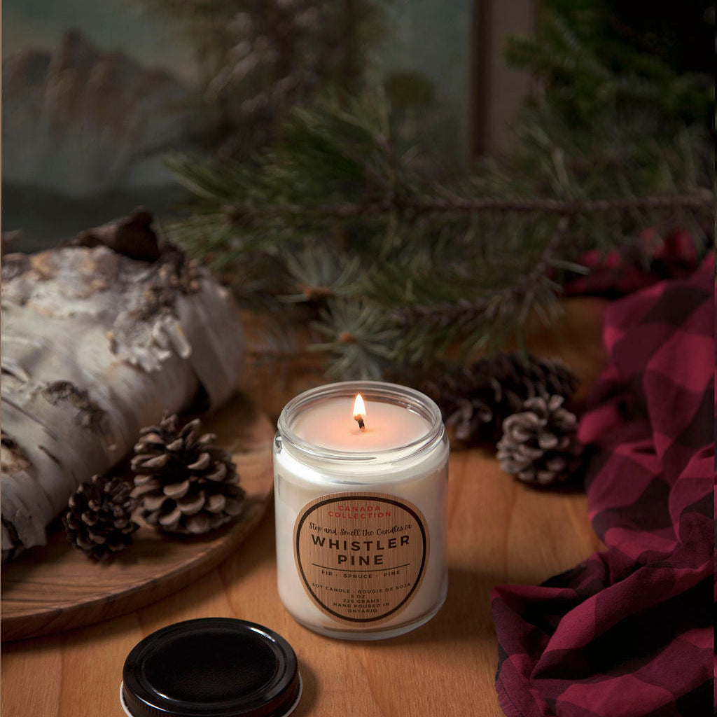 Candle labeled 'Whistler Pine' on a wooden surface with decorative elements.
