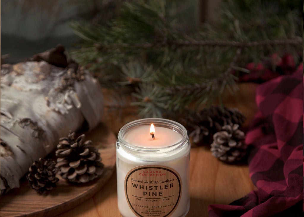 Candle labeled 'Whistler Pine' on a wooden surface with decorative elements.