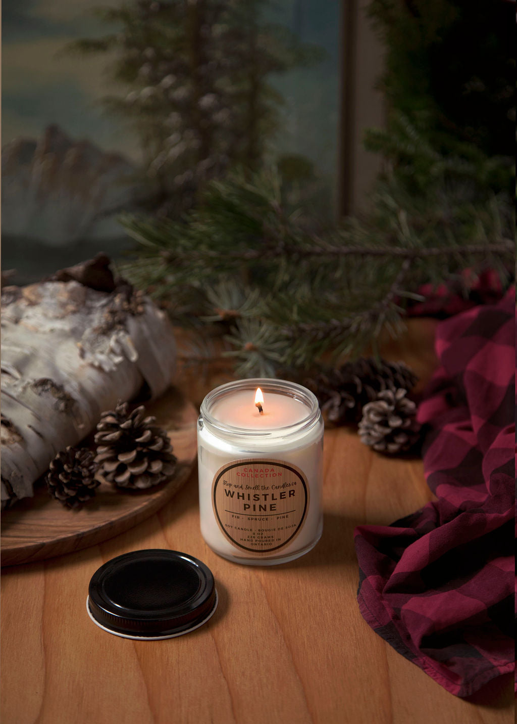 Candle labeled 'Whistler Pine' on a wooden surface with decorative elements.