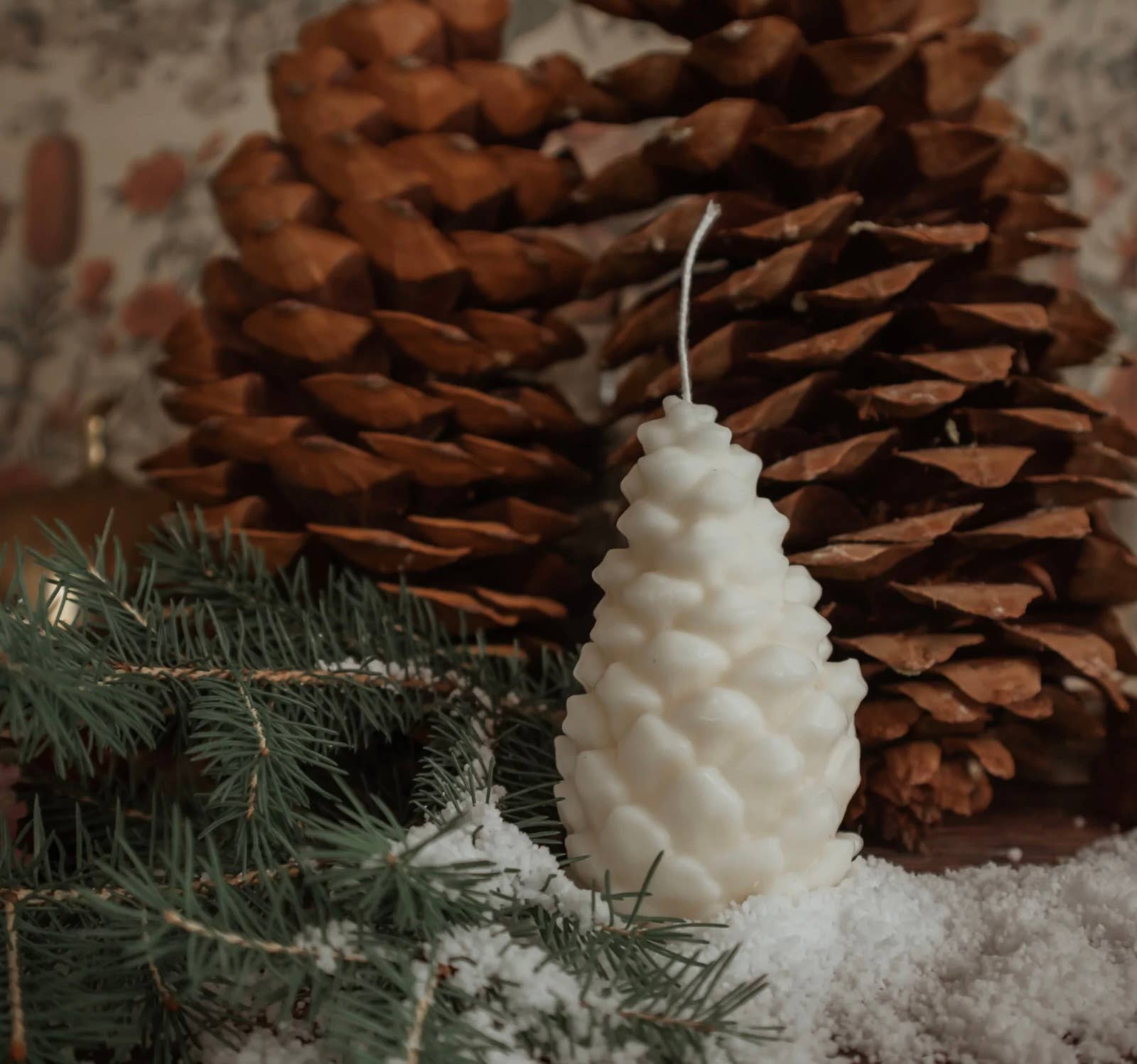 White pillar candle in pinecone shape sitting with real pinecones and pine needles