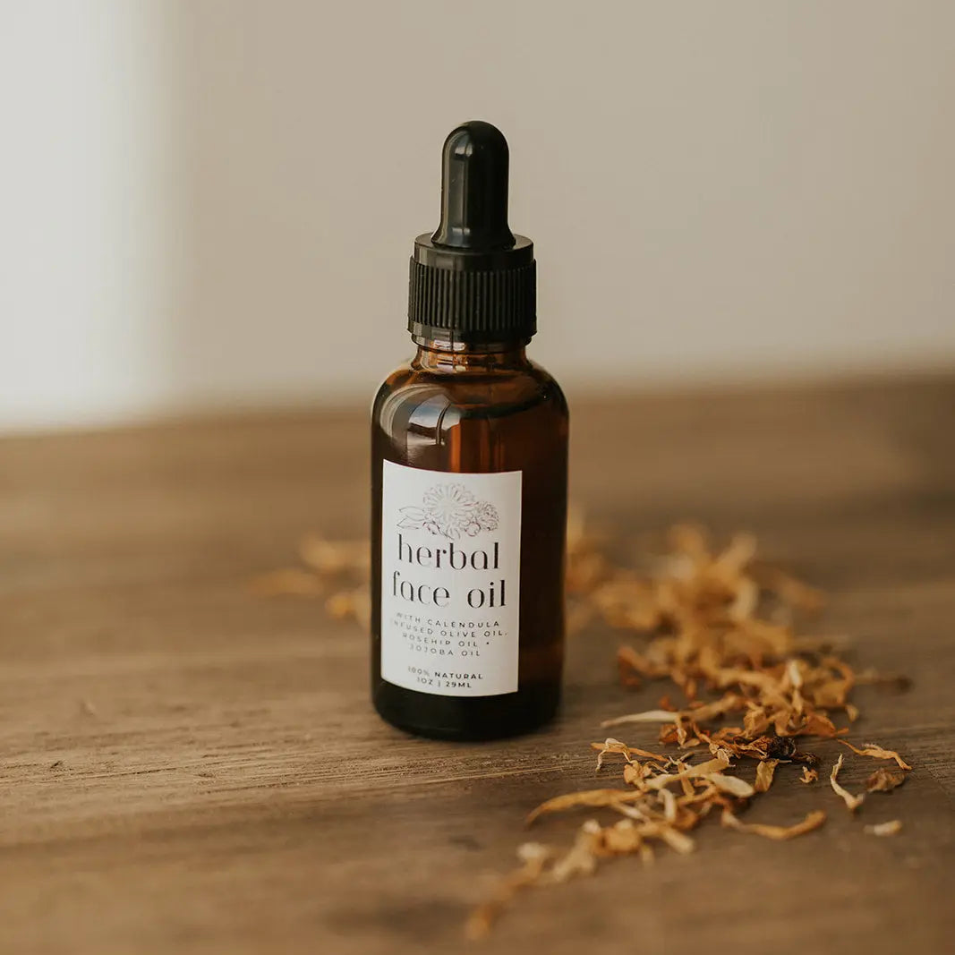 Bottle of herbal face oil on a wooden surface with dried herbs.