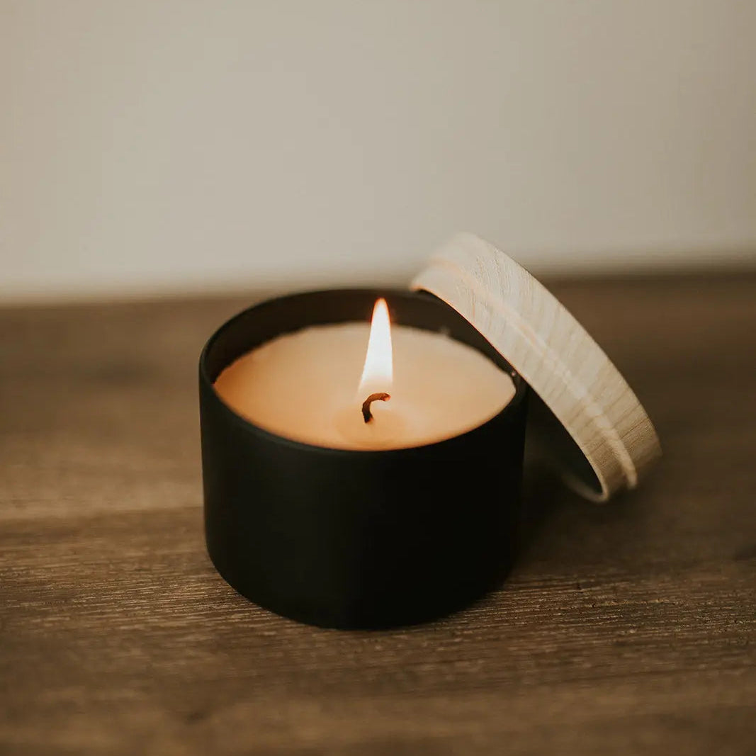 Small black candle with a lit wick on a wooden surface