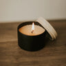 Small black candle with a lit wick on a wooden surface