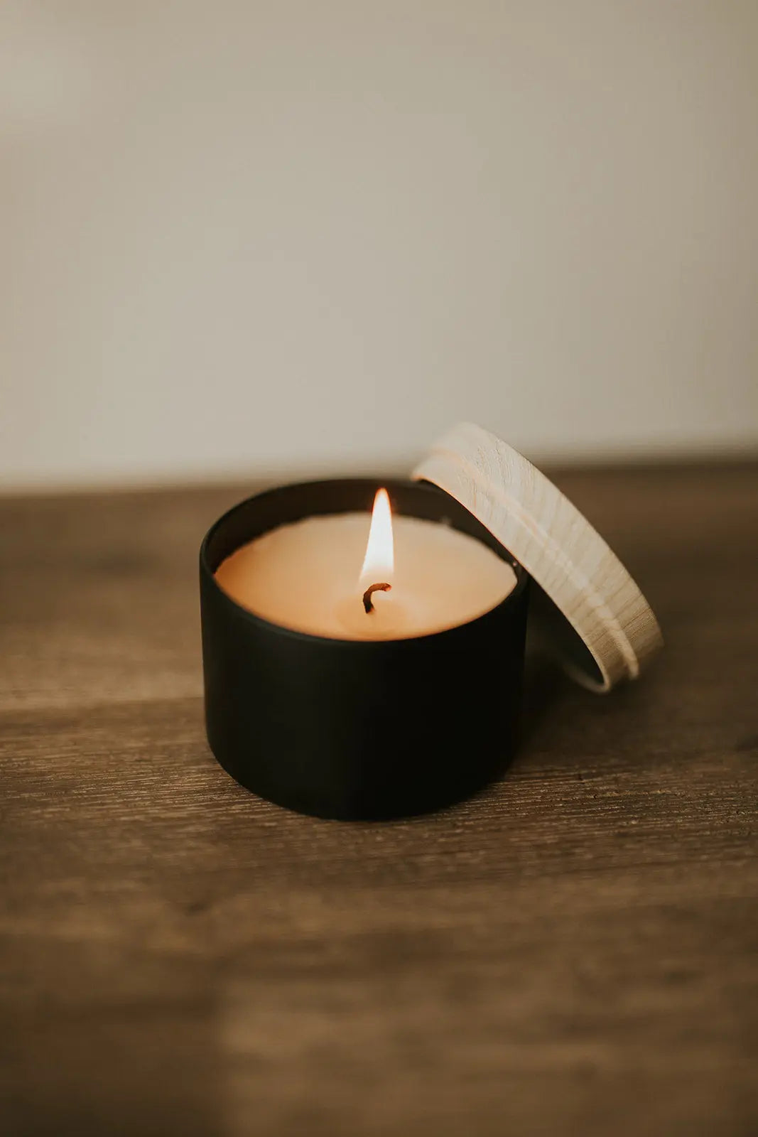 Small black candle with a lit wick on a wooden surface