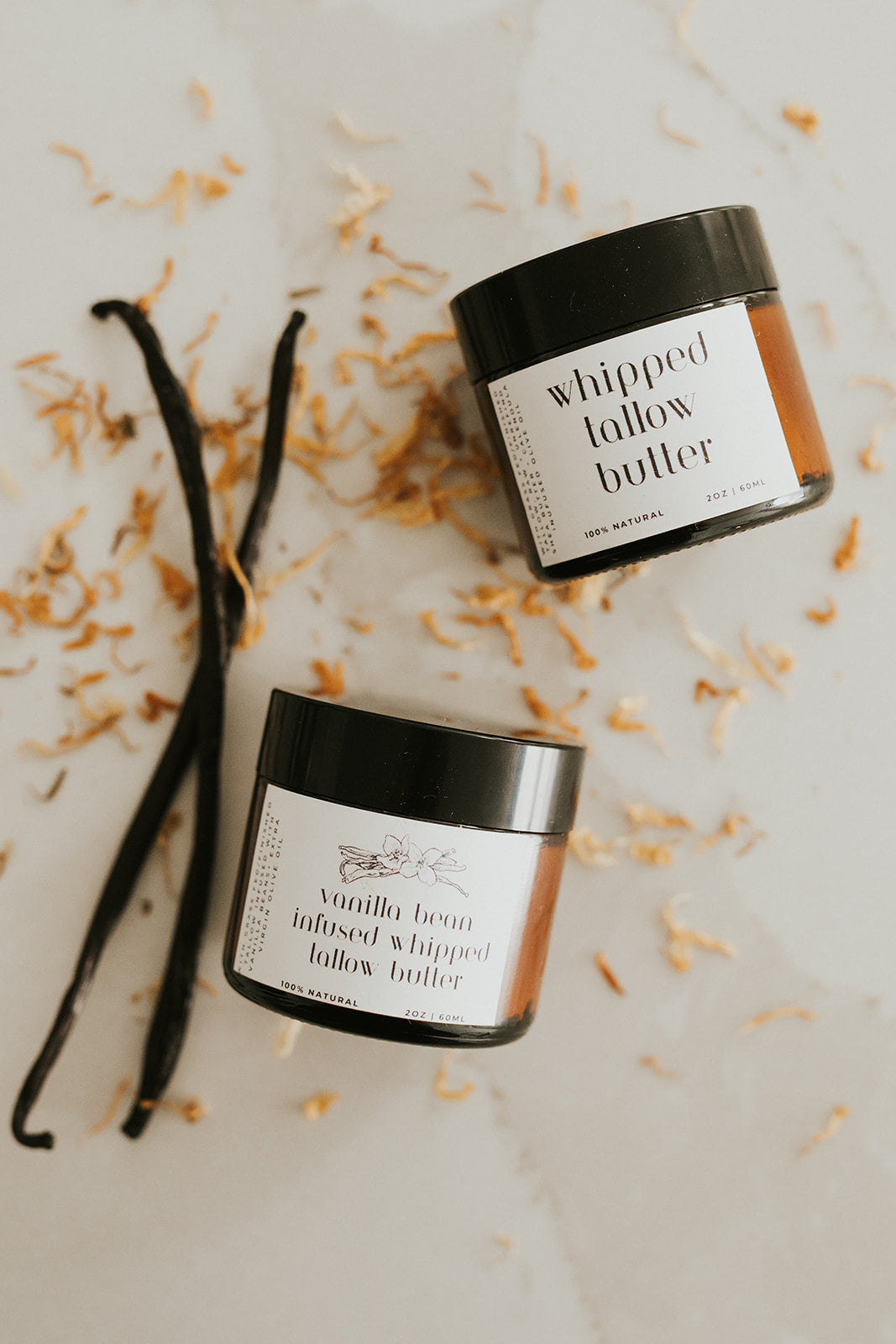 Two jars of 'whipped lallow butter' with vanilla beans on a light background