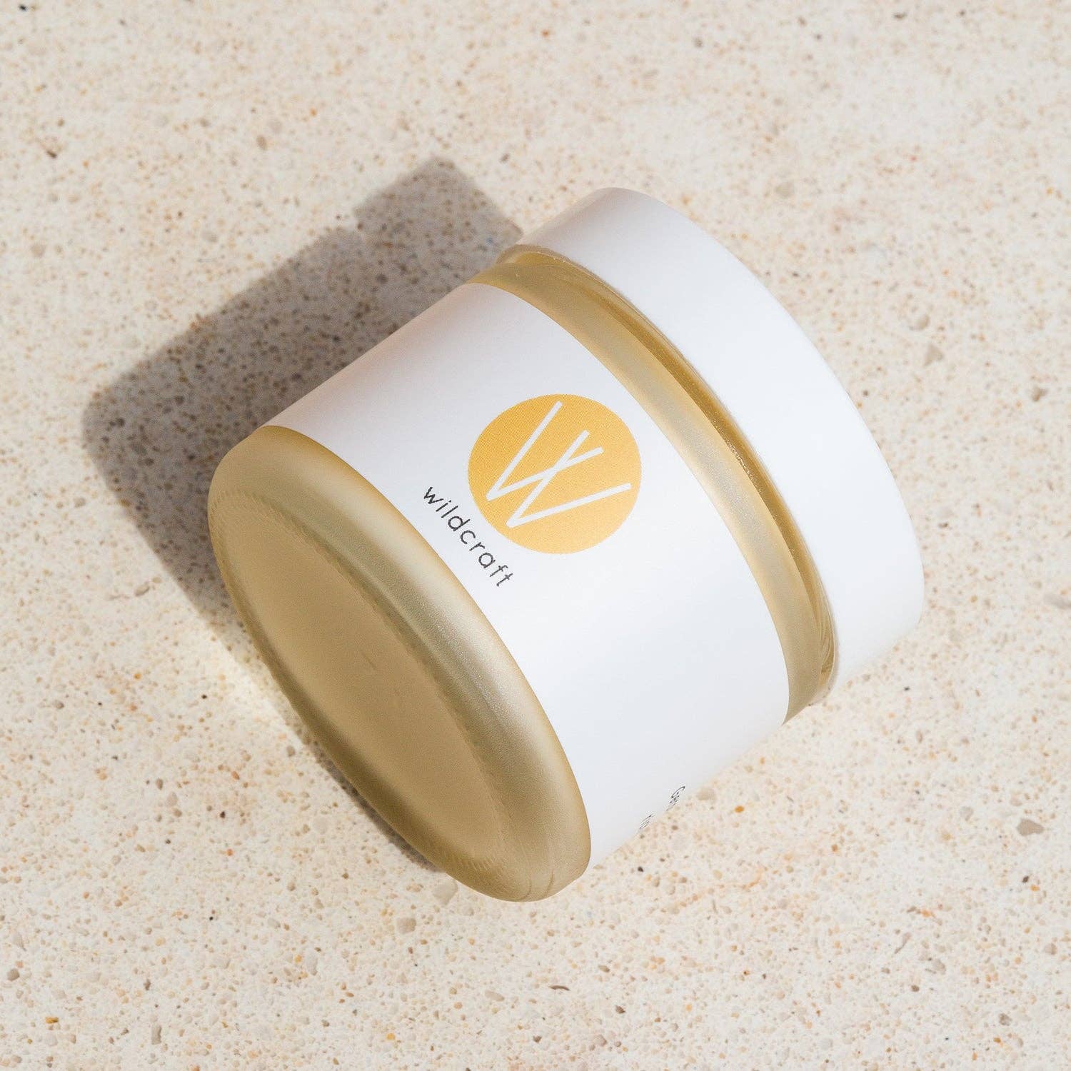 White and gold jar with 'wildcraft' logo on a beige sand background