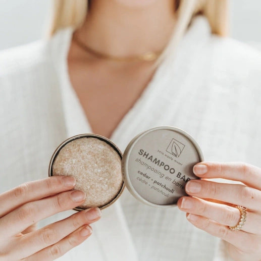 Person holding a shampoo bar in a container, with a neutral background