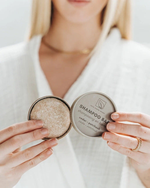 Person holding a shampoo bar in a container, with a neutral background
