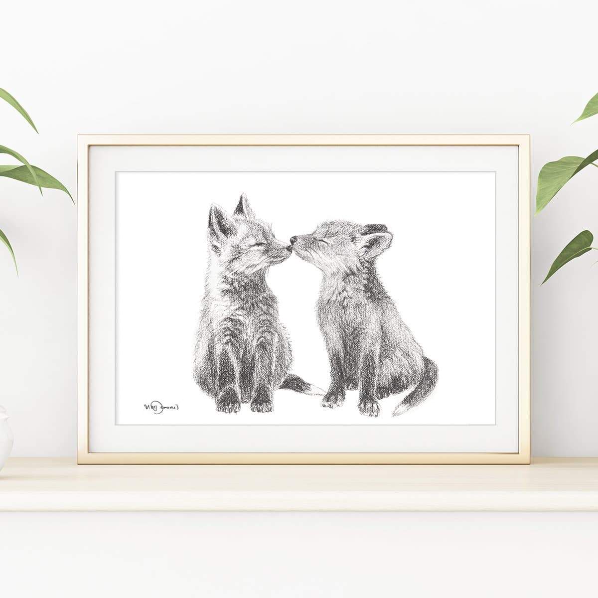 Framed artwork of two foxes kissing on a white wall with plant decorations.