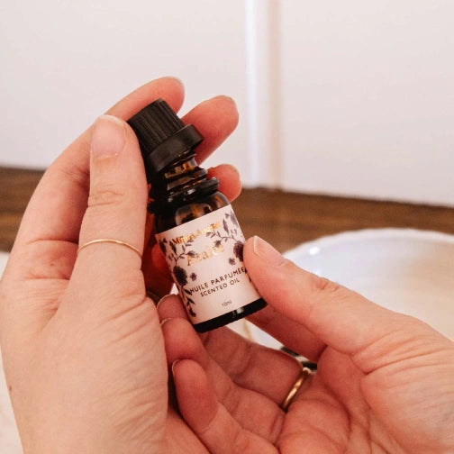Scented oil for relaxation and reflection, Mimi & August Azalée fragrance oil bottle, Hand holding a small bottle of perfume with a floral label on a neutral background