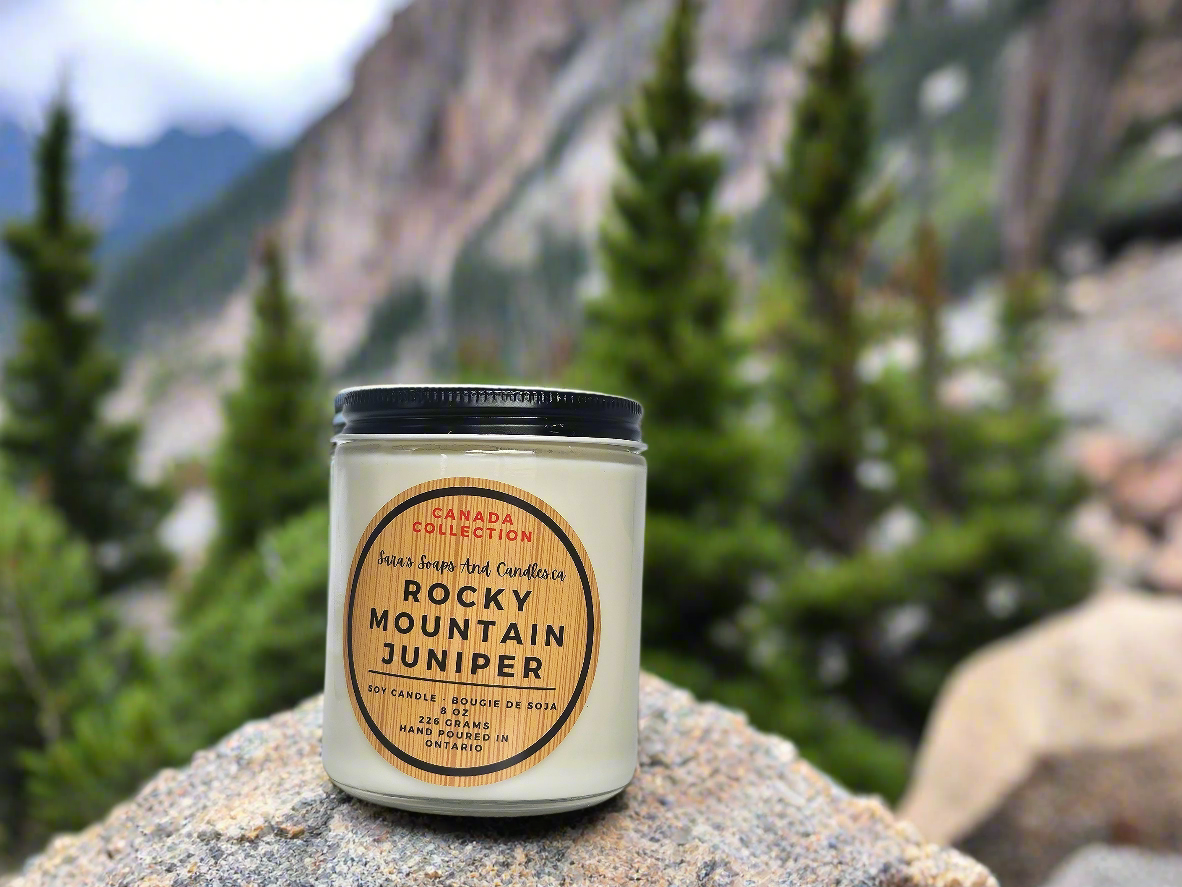 Candle labeled 'Rocky Mountain Juniper' on a rock with a mountainous background