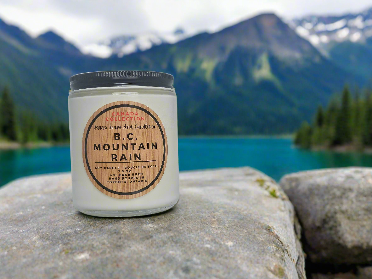Candle labeled 'B.C. Mountain Rain' on a rock with a mountain and lake background
