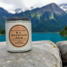 Candle labeled 'B.C. Mountain Rain' on a rock with a mountain and lake background
