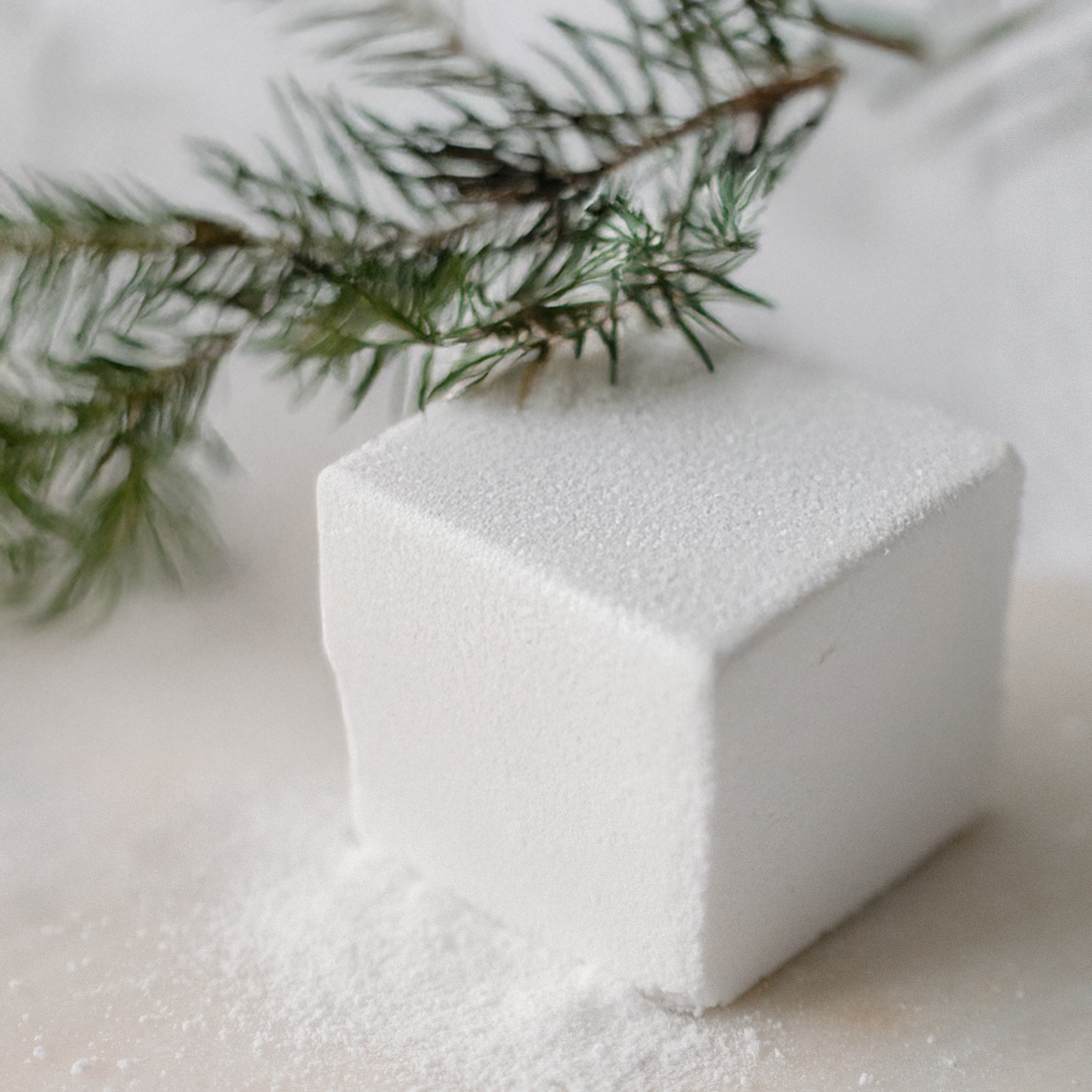 White cube on a snowy surface with a branch in the background