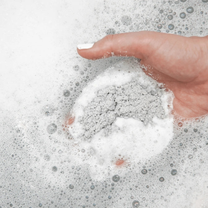 Hand interacting with soapy water on a light gray background