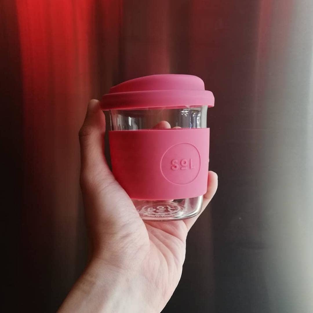 Hand holding a pink 8OZ Radiant Rosé glass travel tumbler from SOL Cups, highlighting its eco-friendly design.