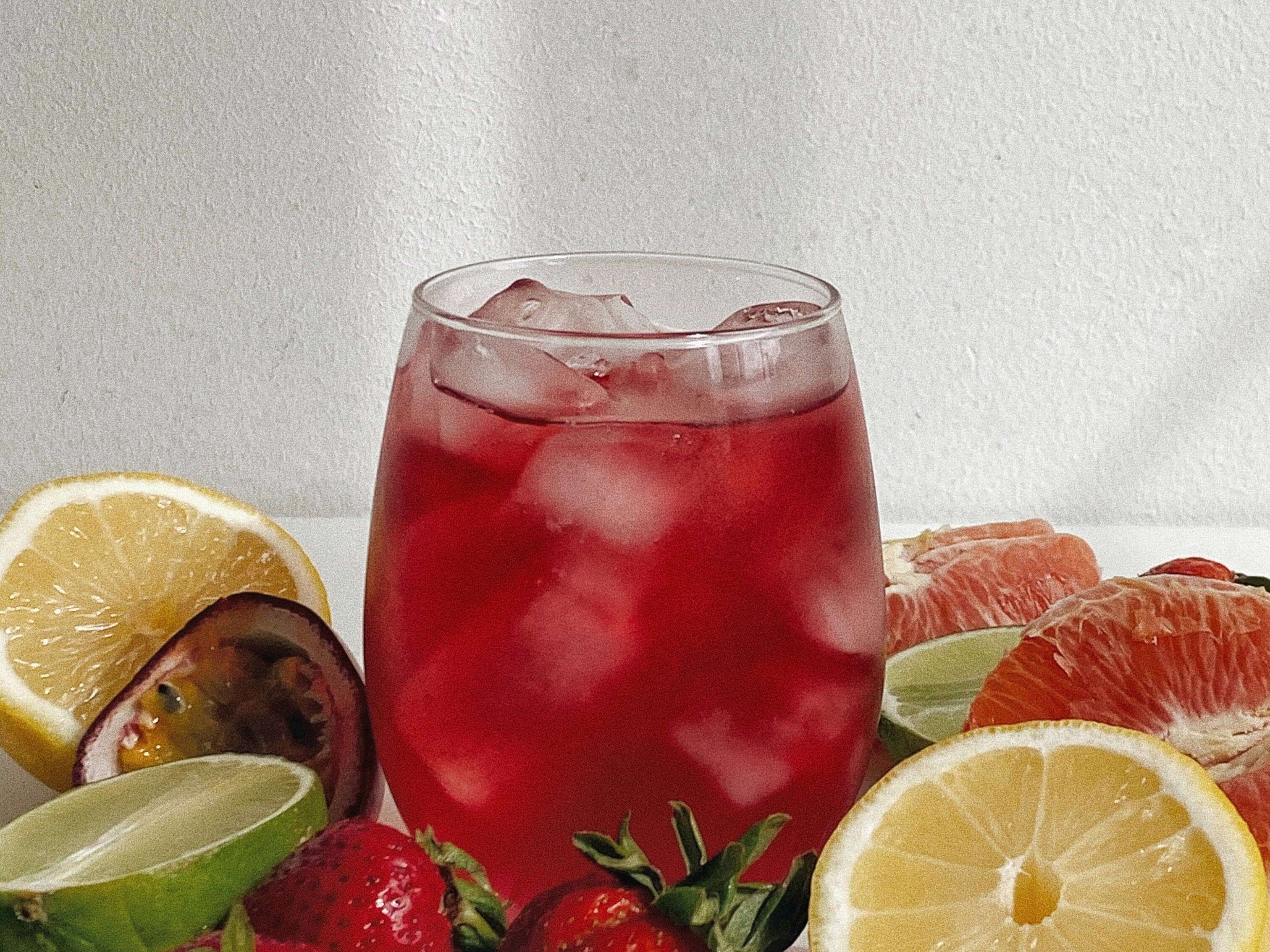 Refreshing rose hibiscus superfood tea with ice, surrounded by fresh fruits like strawberries and citrus slices.