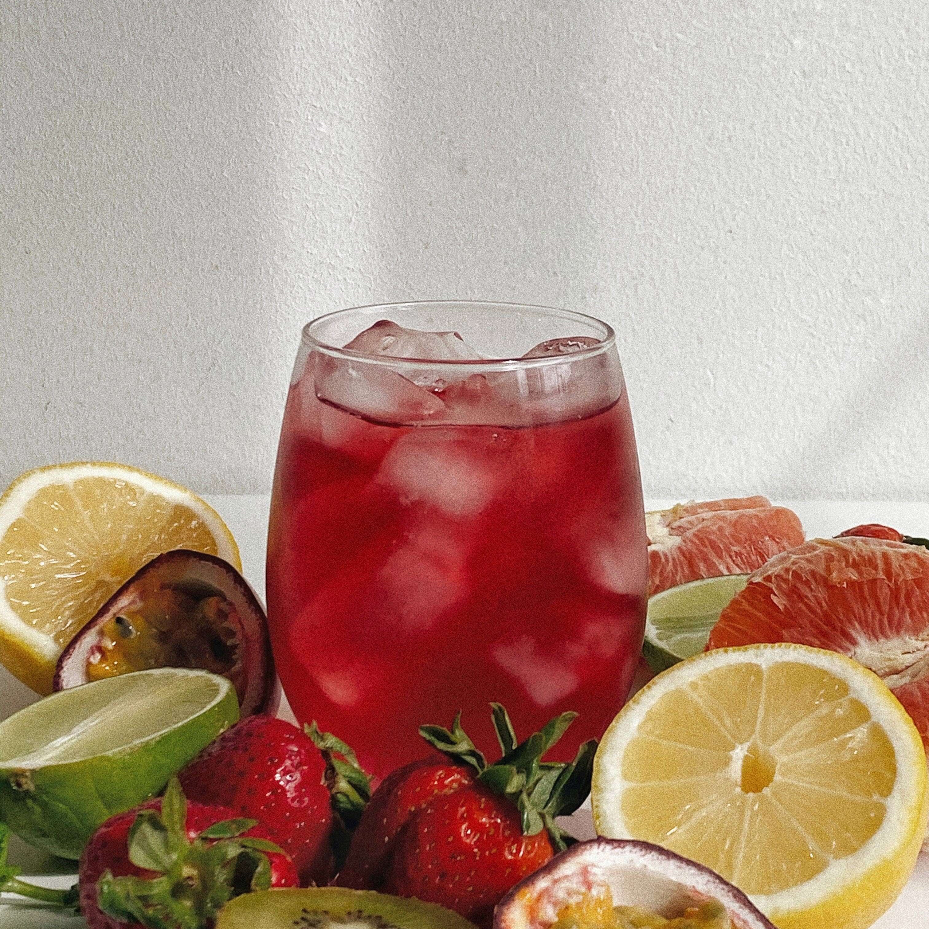 Refreshing rose hibiscus superfood tea with ice, surrounded by fresh fruits like strawberries and citrus slices.