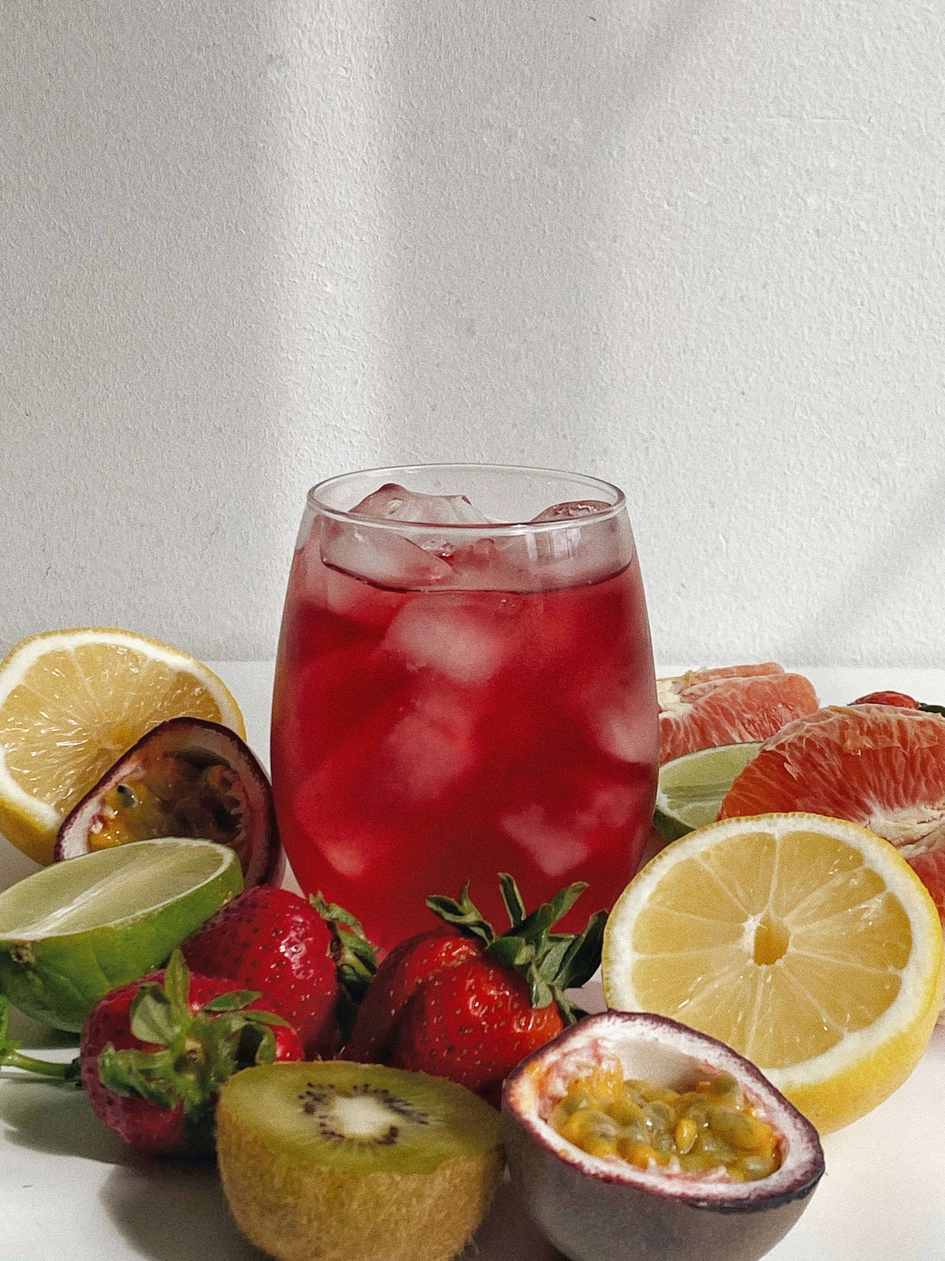 Refreshing rose hibiscus superfood tea with ice, surrounded by fresh fruits like strawberries and citrus slices.