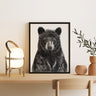 Framed black and white bear artwork on a wall above a wooden table with decorative items.