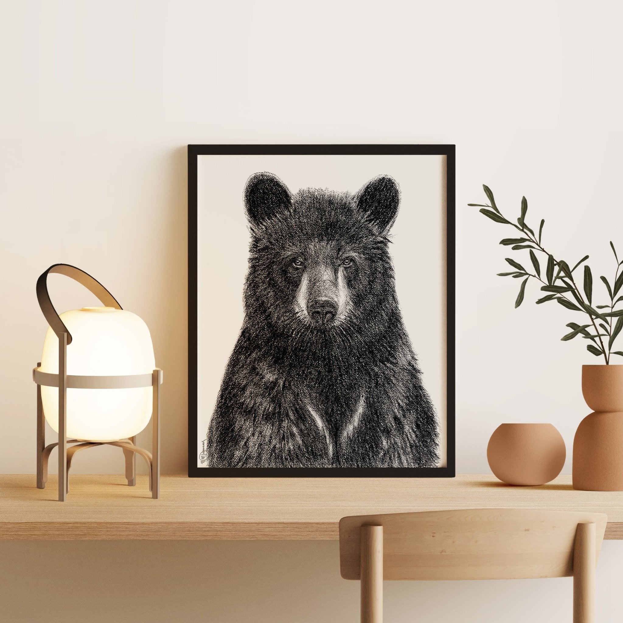 Framed black and white bear artwork on a wall above a wooden table with decorative items.