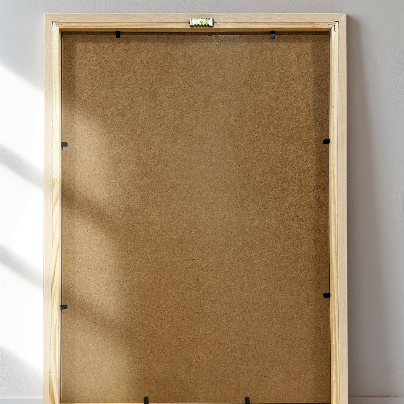 Wooden picture frame on a white wall with sunlight casting shadows.