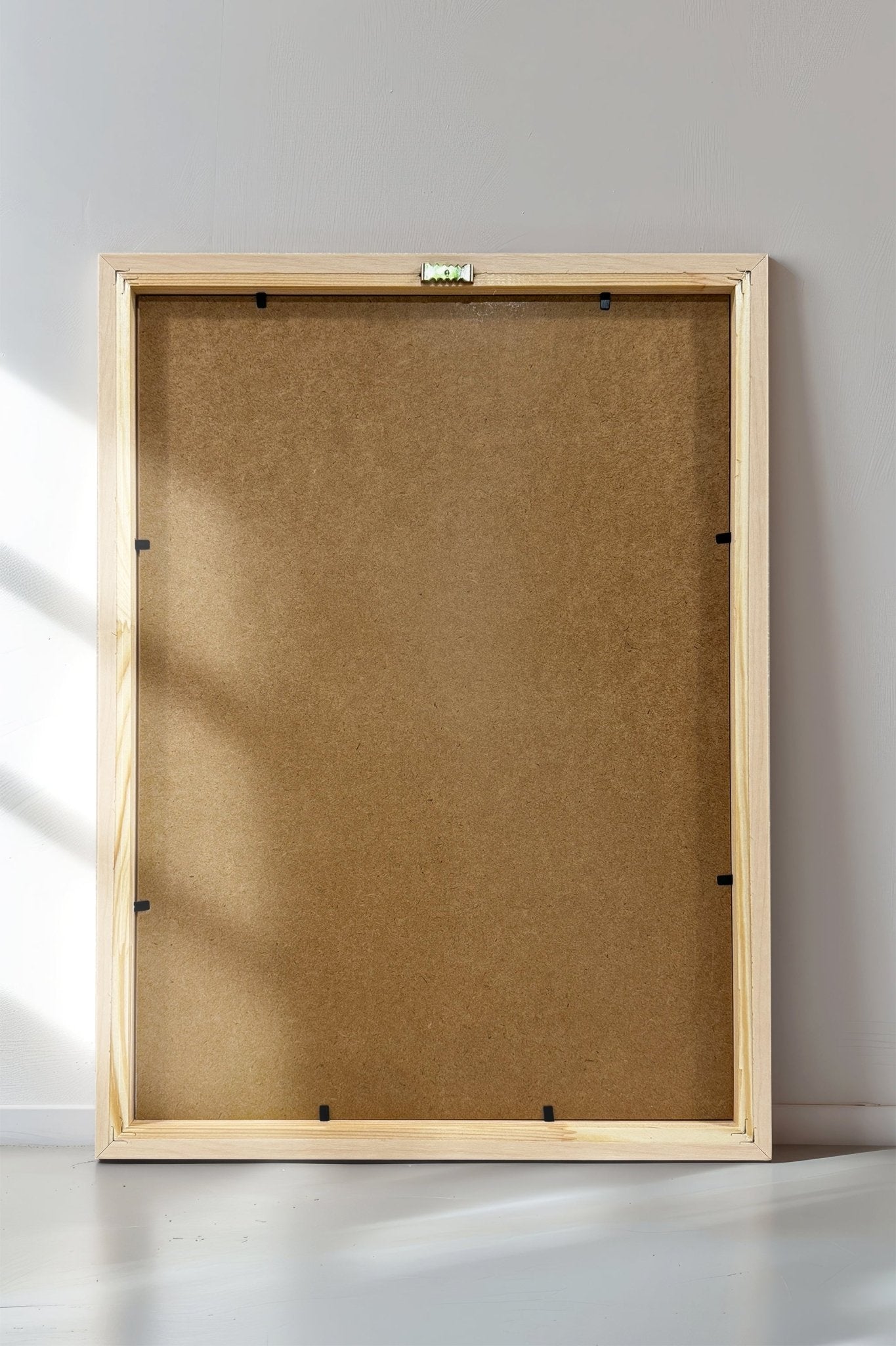 Wooden picture frame on a white wall with sunlight casting shadows.