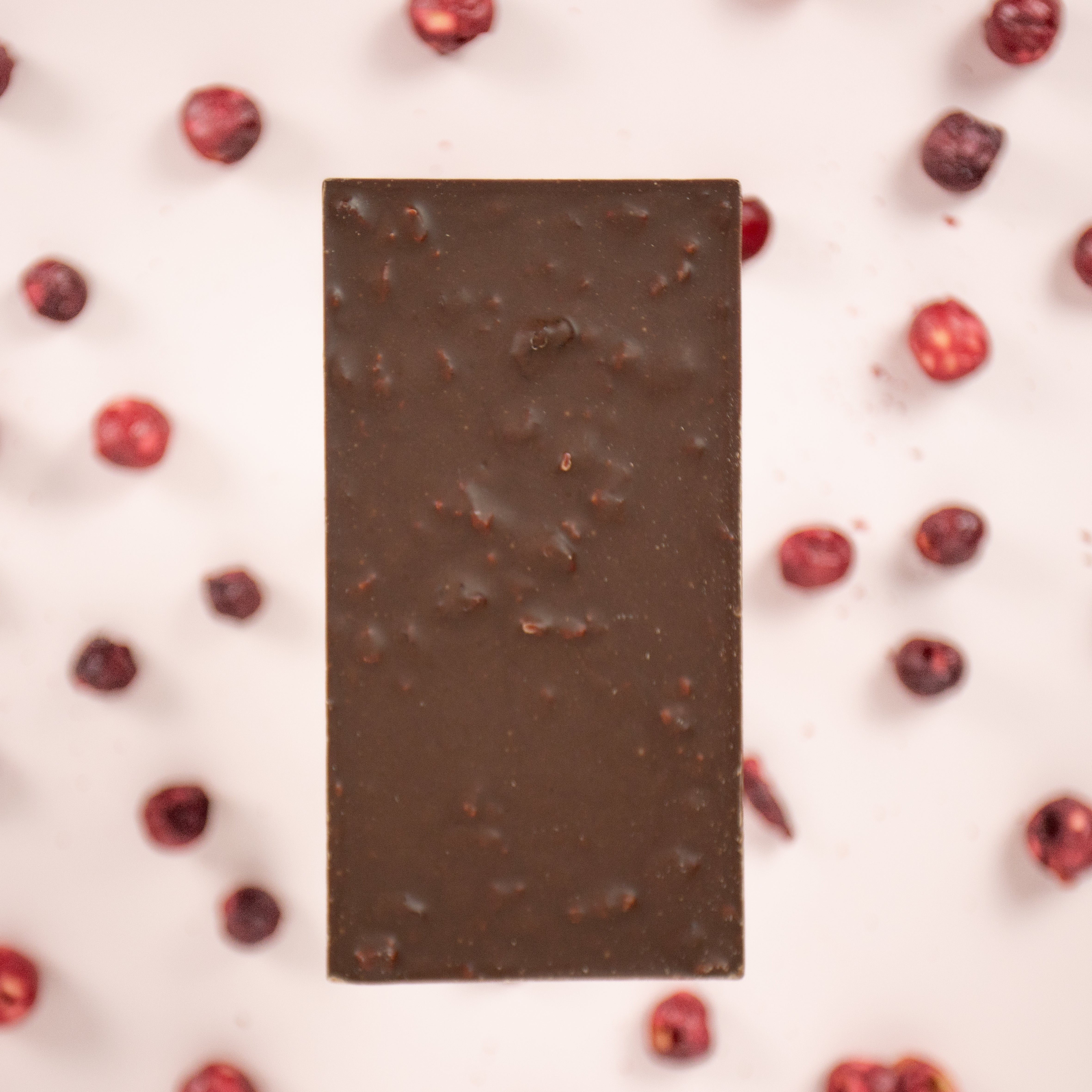 Dark chocolate bar with cranberries on a light pink background
