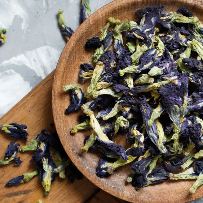 Dried butterfly pea flowers in a wooden bowl on a wooden surface. The Sobr Market
