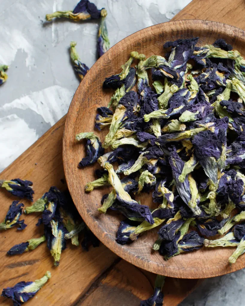 Dried butterfly pea flowers in a wooden bowl on a wooden surface. The Sobr Market