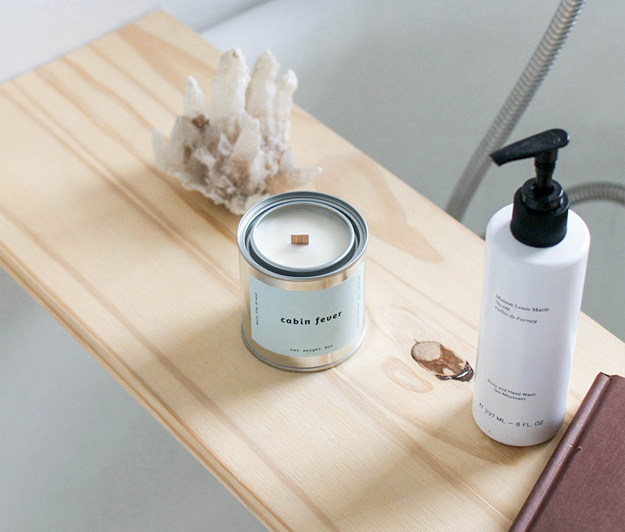 Candle and bottle on a wooden tray with a neutral background