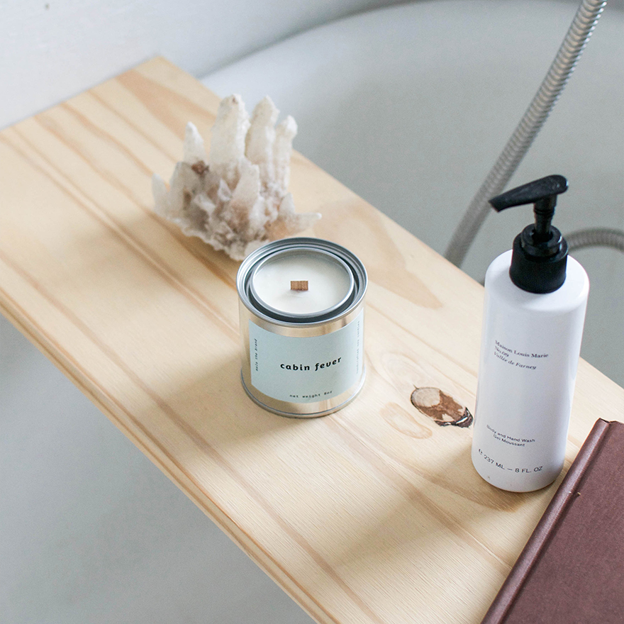 Candle and bottle on a wooden tray with a neutral background