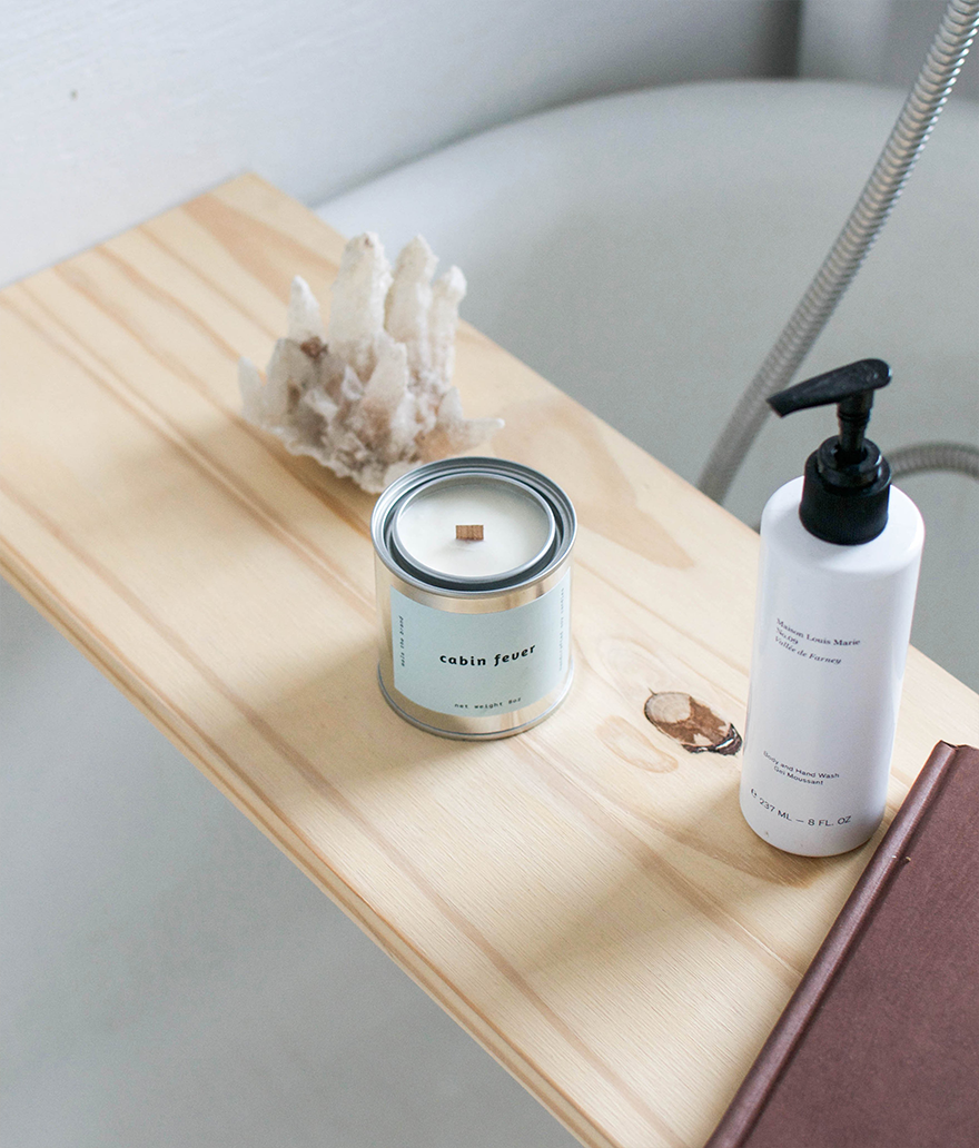 Candle and bottle on a wooden tray with a neutral background