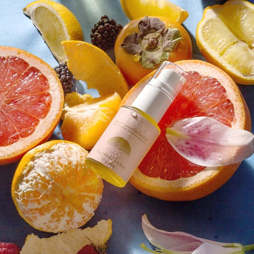 Skincare product bottle surrounded by sliced fruits and flowers on a blue background Aurora Cardea AuSet facial Oil