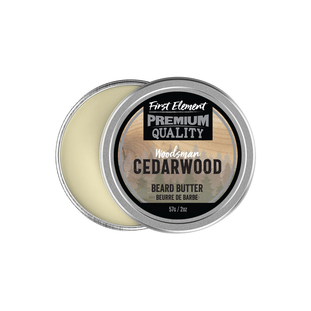 An open round metal tin of First Element Cedarwood Beard Butter, showing the pale cream-colored balm inside and a label with a woodgrain pattern on a white background.