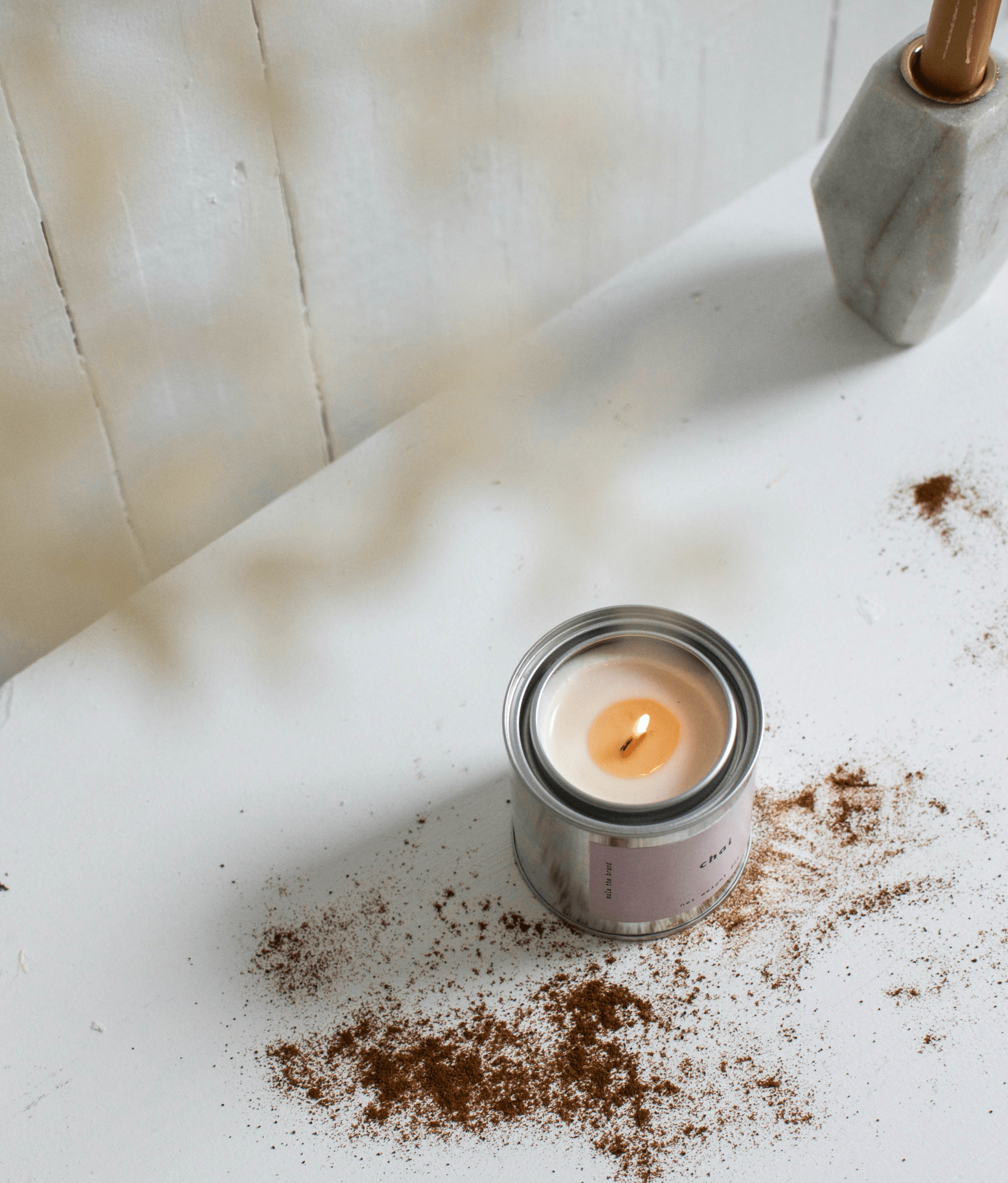 Candle in a metal can on a white surface with cinnamon spice around it