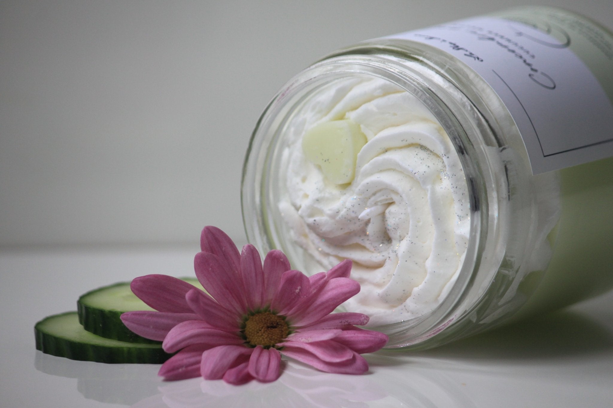 Jar of white cream with a pink flower and cucumber slices on a white background