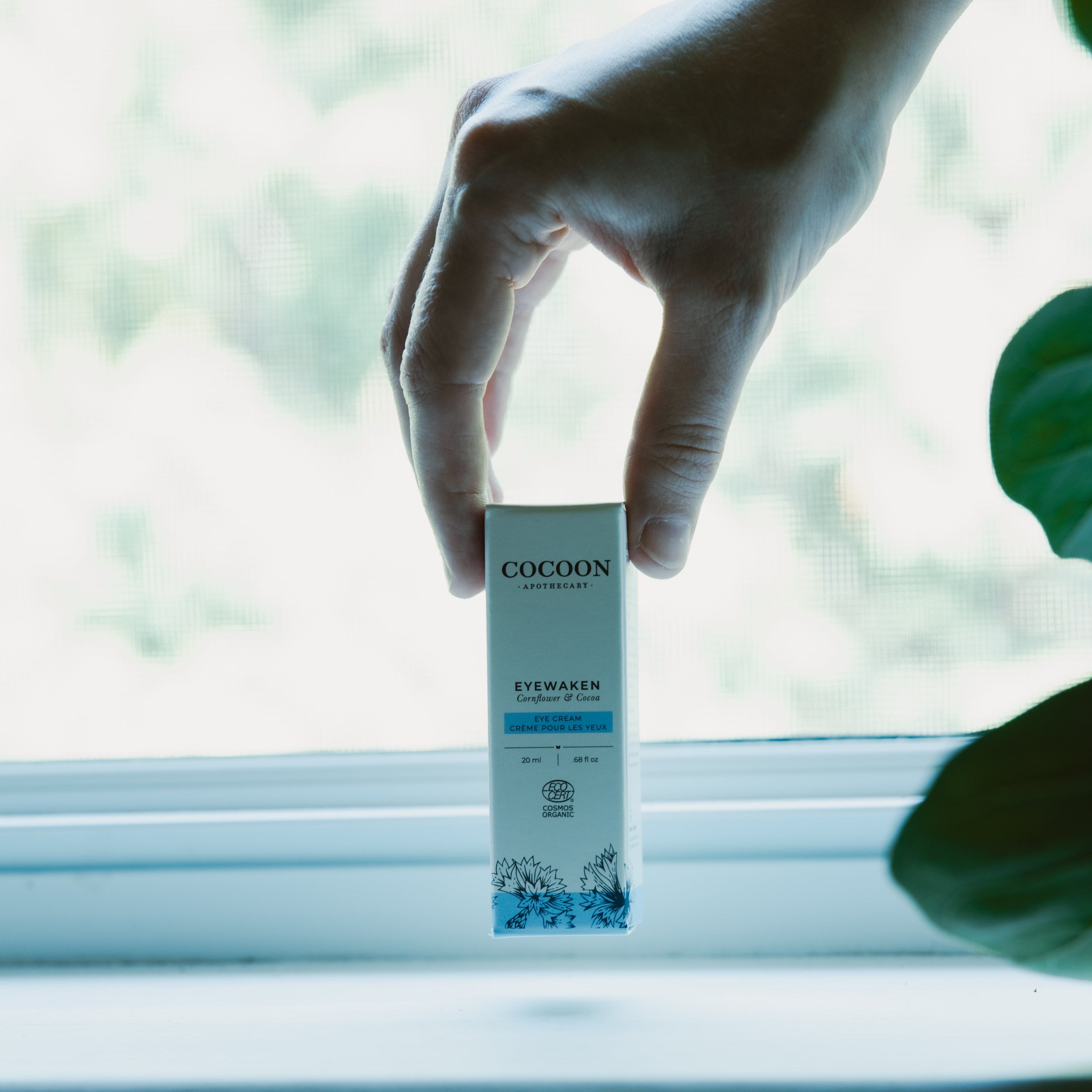 Cocoon skincare product held by a hand with a blurred natural background