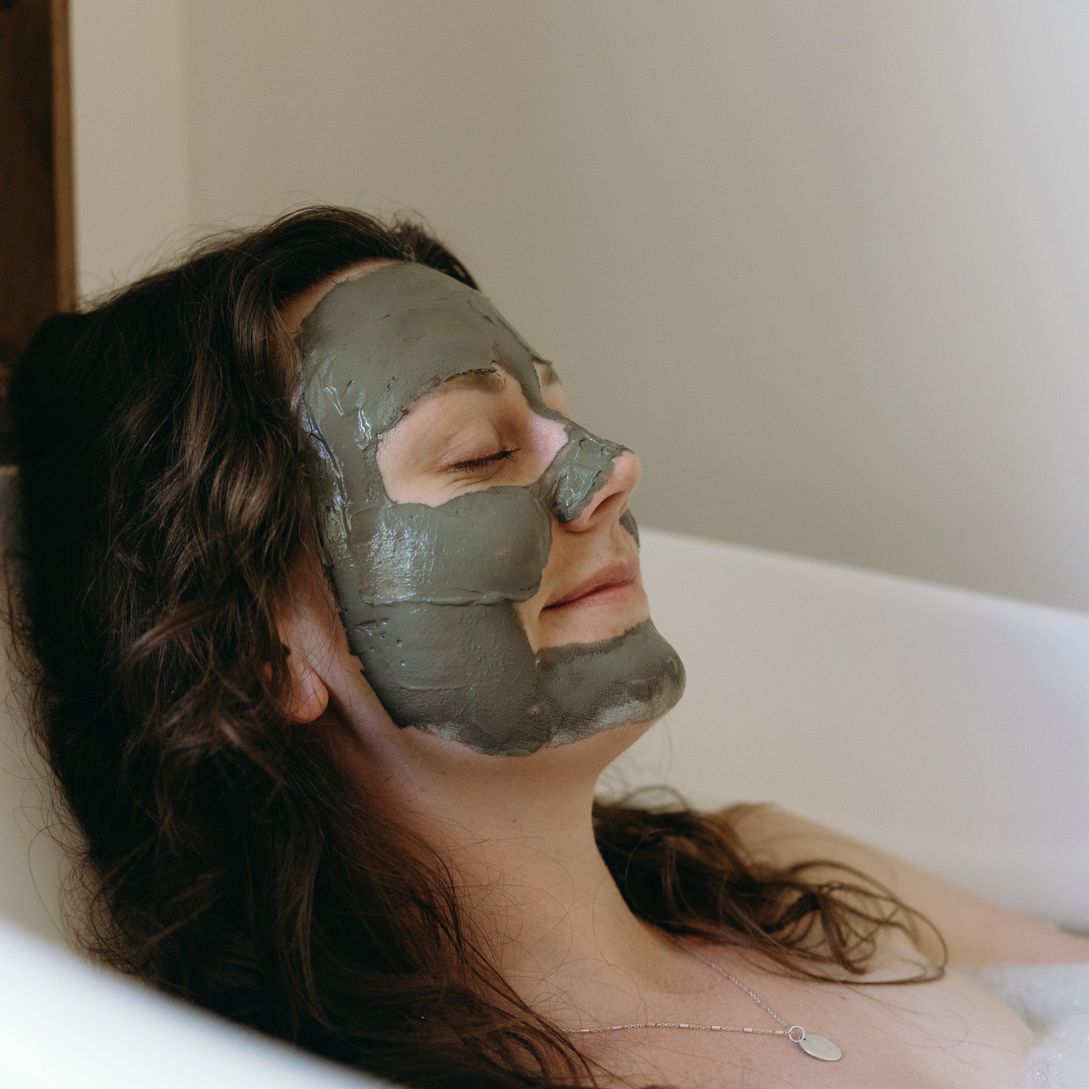 Woman with a clay face mask lying in a bathtub