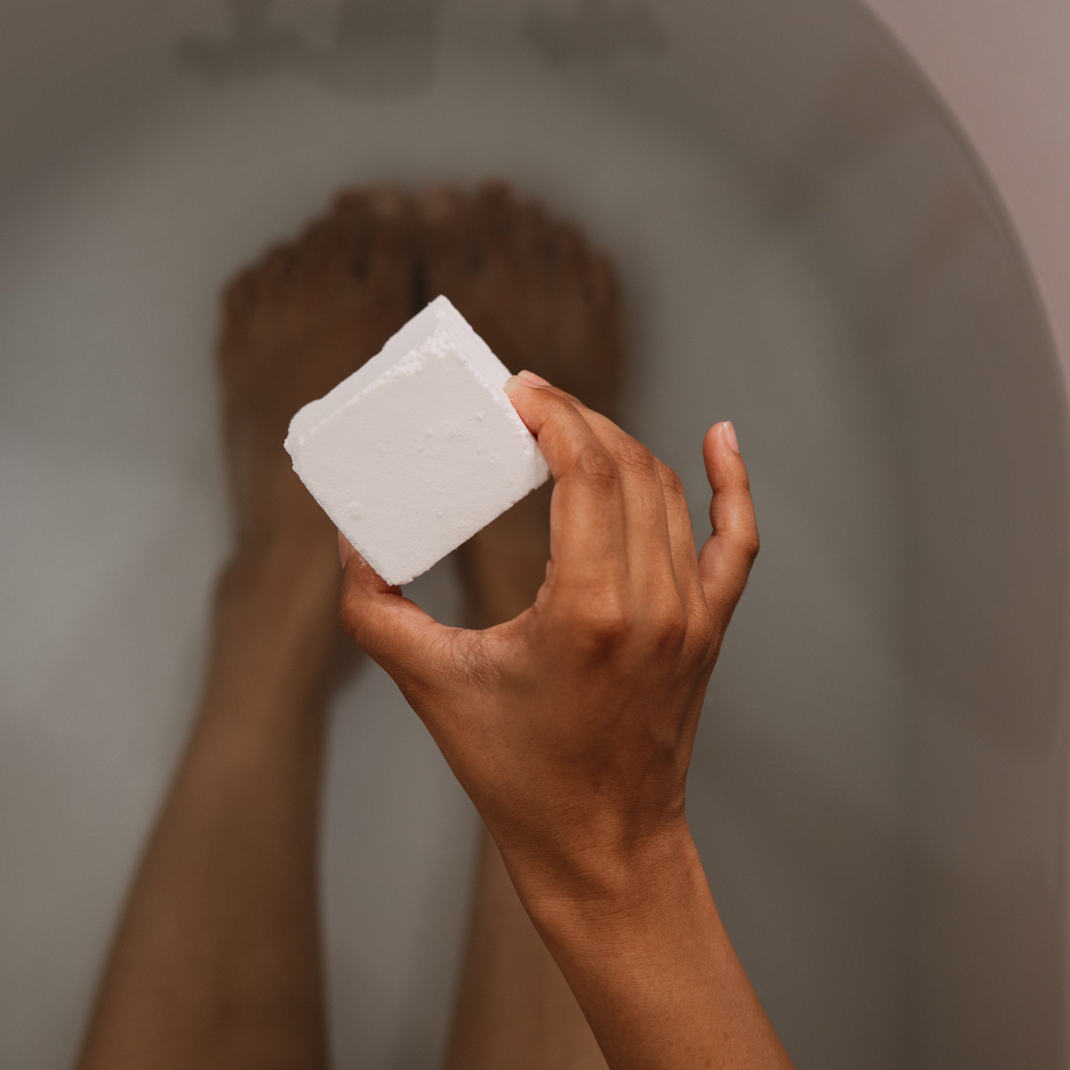 Hand holding a bar of soap above a bathtub