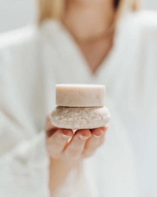 Person holding a small, round, beige container with a textured surface against a blurred background