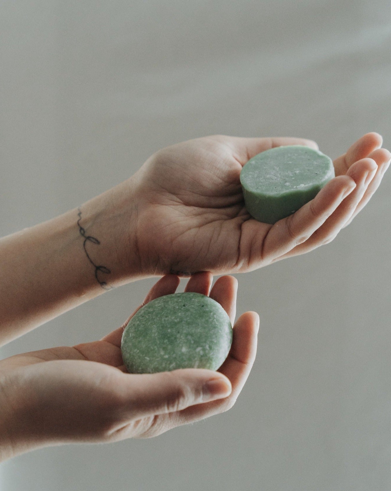 Two hands holding green soap bars against a neutral background
