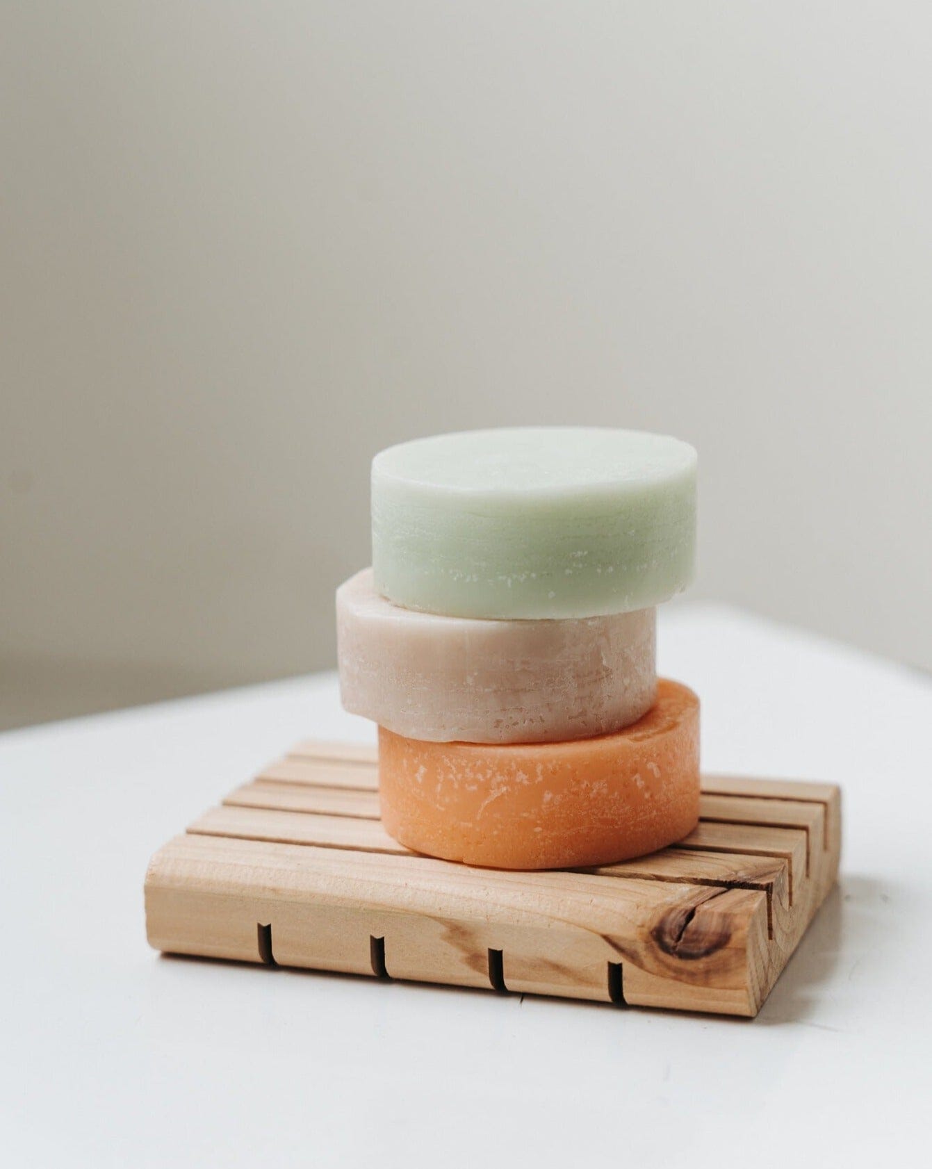 Three stacked soap bars on a wooden soap dish with a neutral background