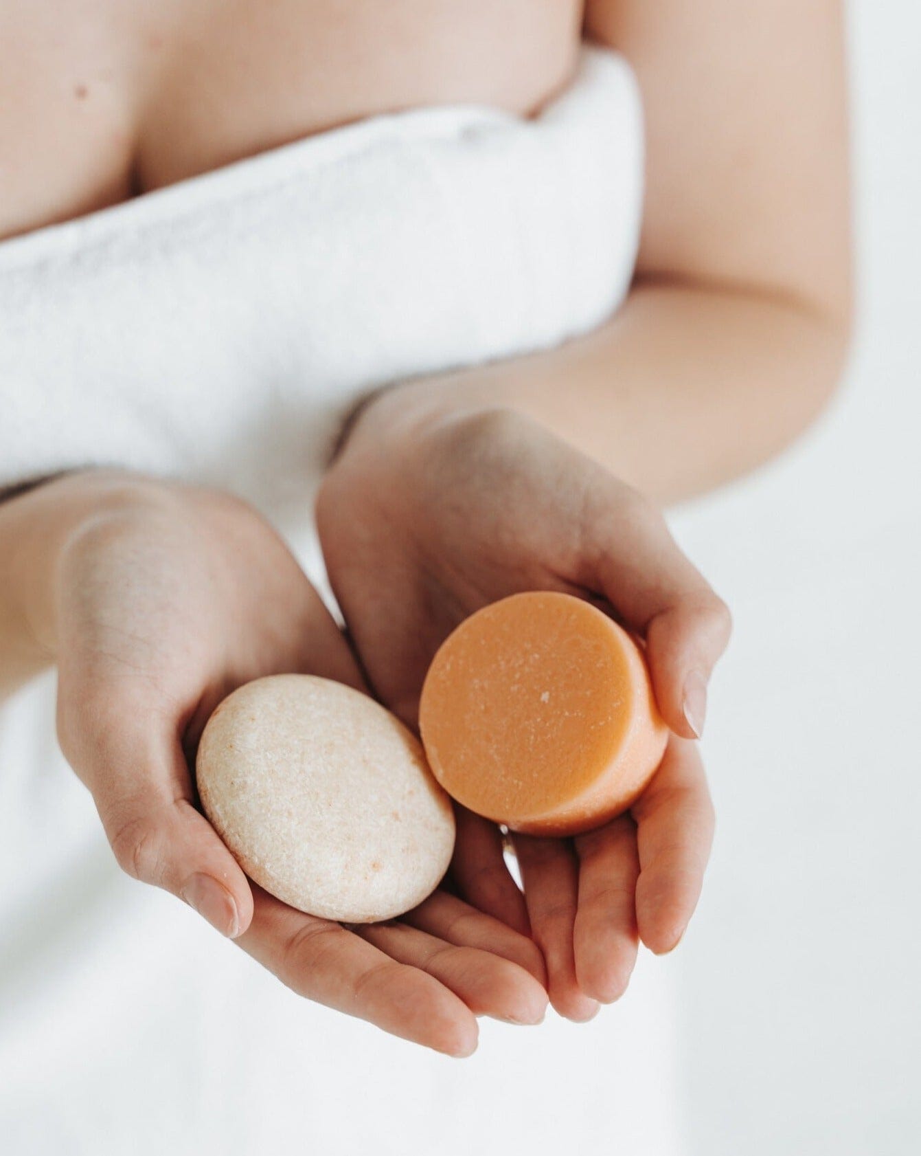 Two soap bars, one white and one orange, held in a person's hands against a white background.