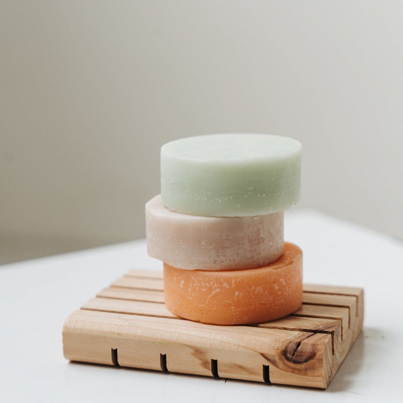 Three stacked soap bars on a wooden soap dish with a neutral background
