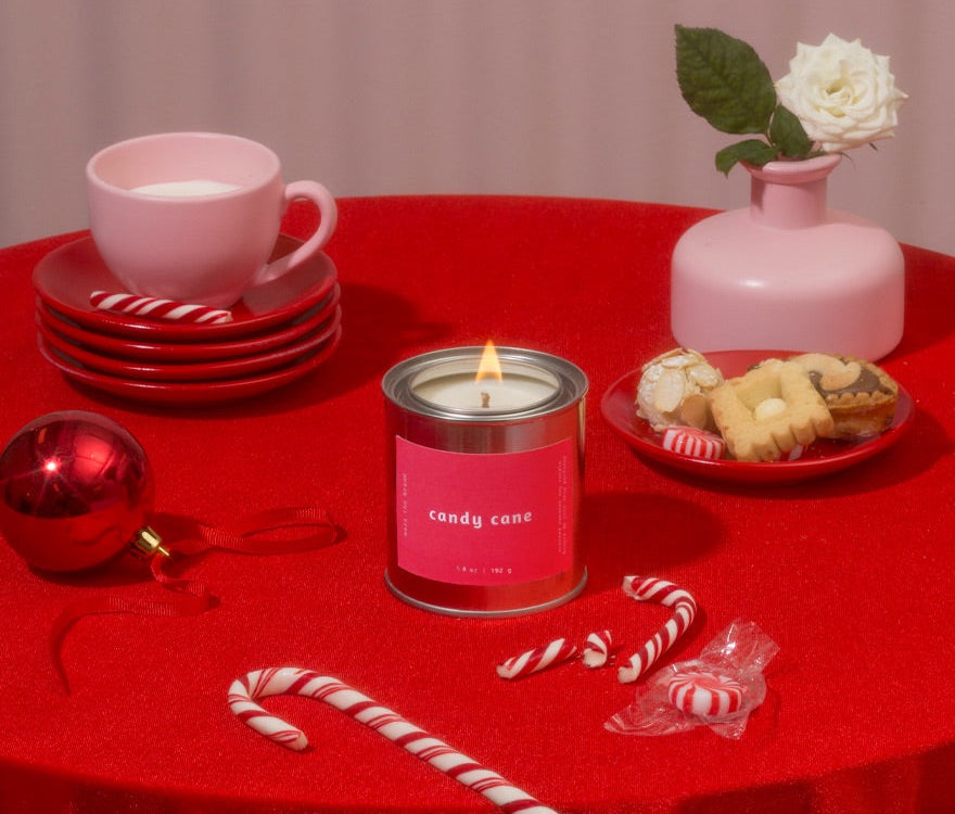 Red tablecloth-covered table with a pink candle, candy canes, cookies, and a pink cup.