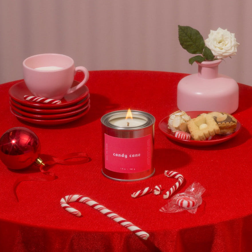 Red tablecloth-covered table with a pink candle, candy canes, cookies, and a pink cup.