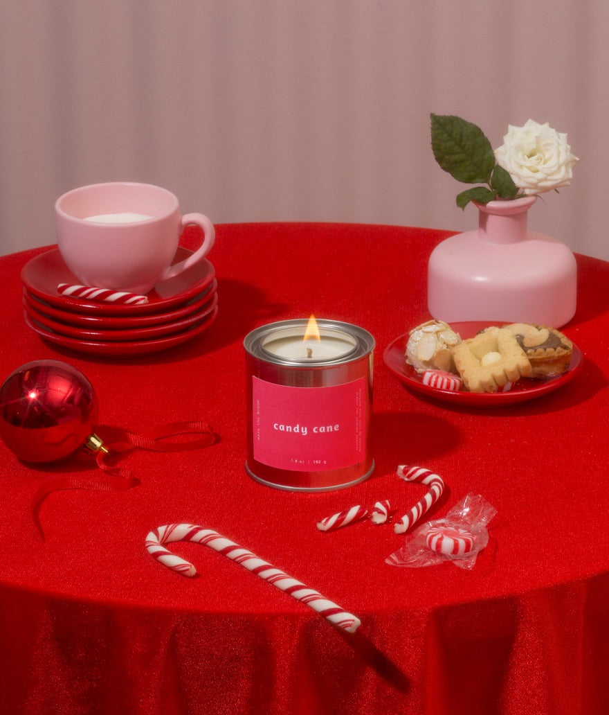 Red tablecloth-covered table with a pink candle, candy canes, cookies, and a pink cup.