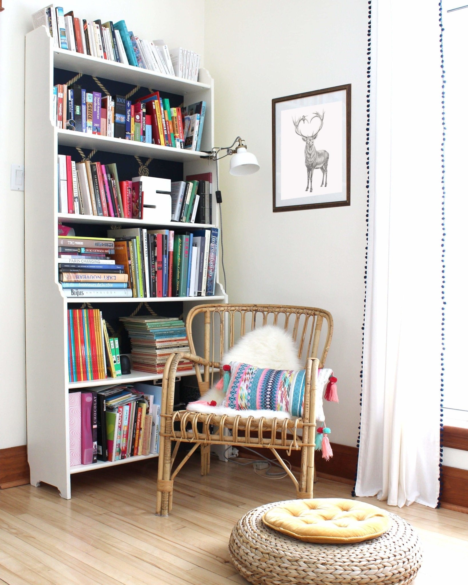 White bookshelf filled with books next to a wicker chair with a colorful pillow in a room.