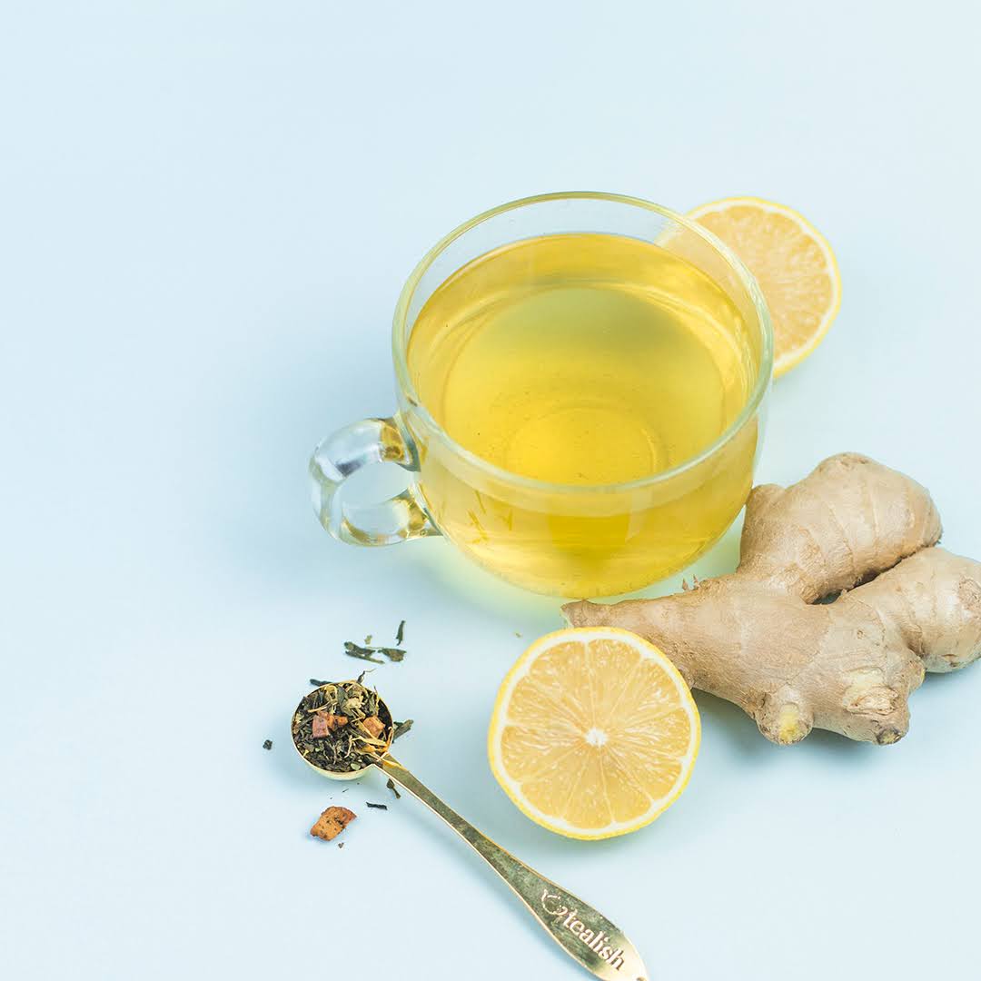Clear glass mug with yellow liquid, lemon slices, and ginger root on a light blue background